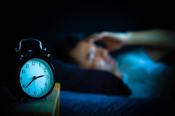 Man struggling with insomnia, awake at night with alarm clock.