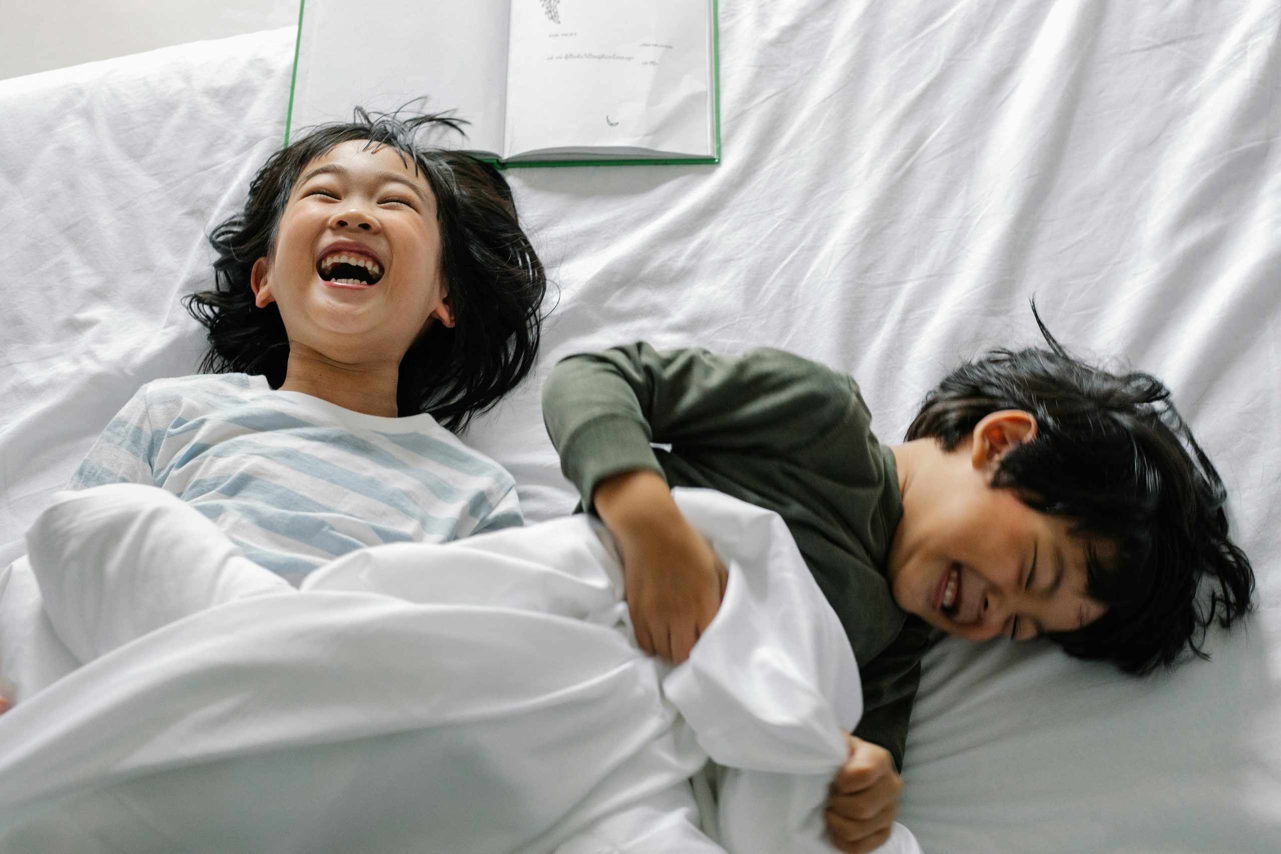 Two happy children laughing while lying on a white bed.