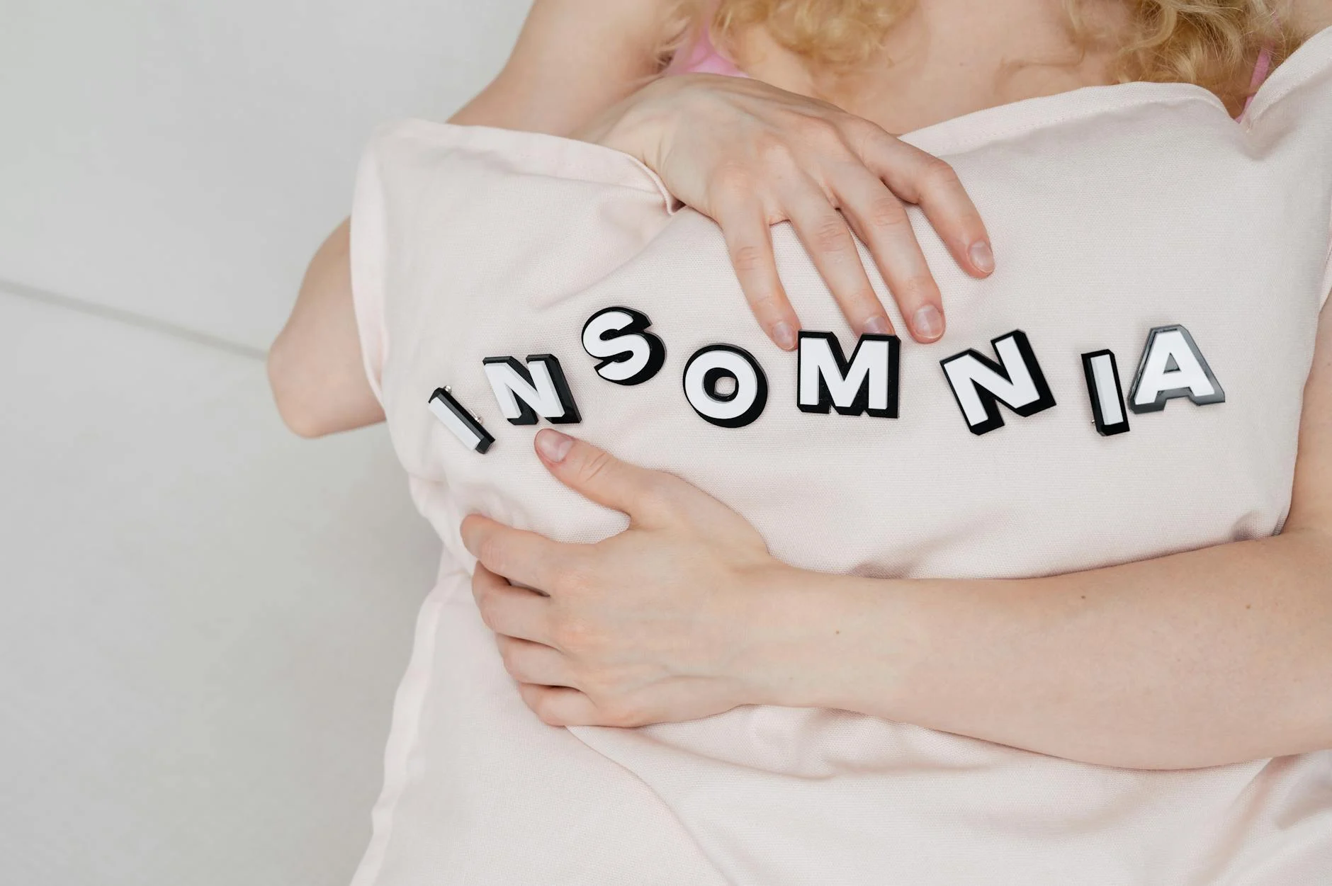 Woman hugging a pillow with the word "INSOMNIA" on it.