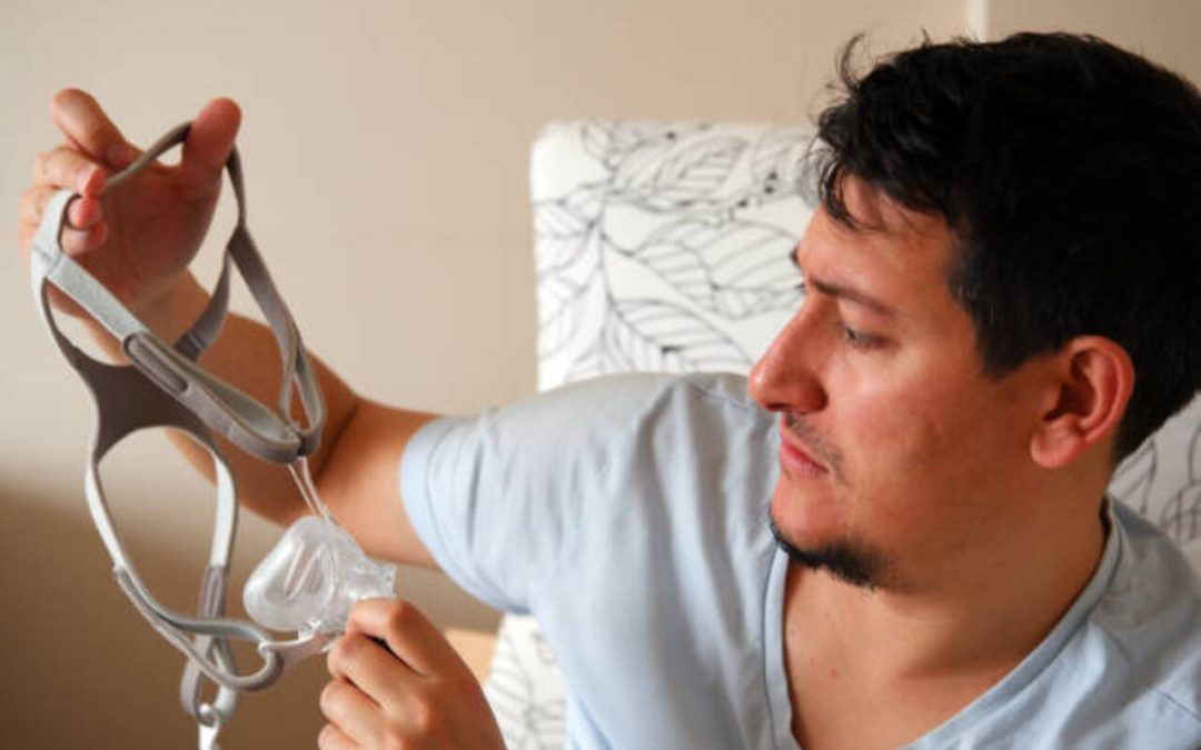 Man holding a CPAP mask for sleep apnea treatment at home.