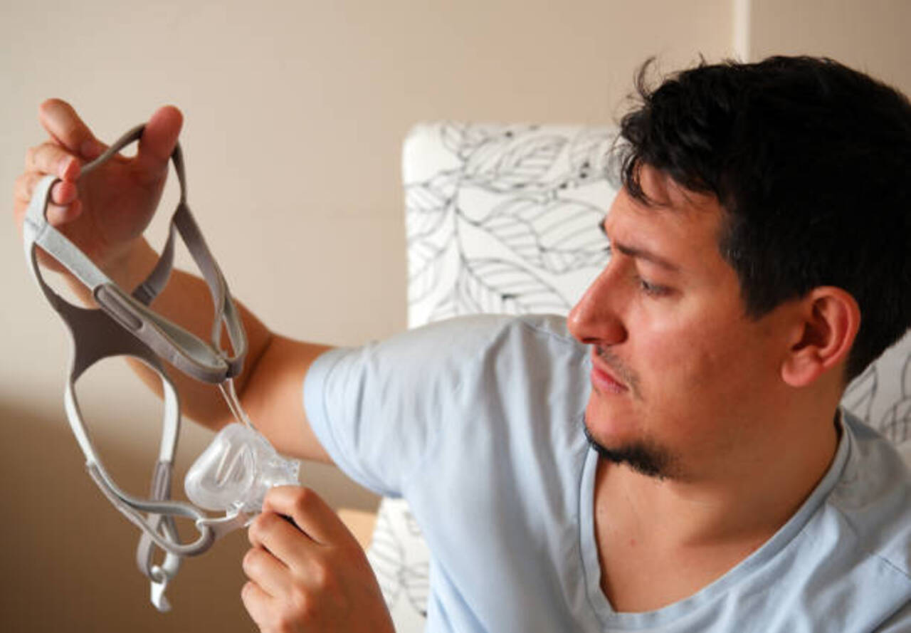 Man holding a CPAP mask for sleep apnea treatment at home.