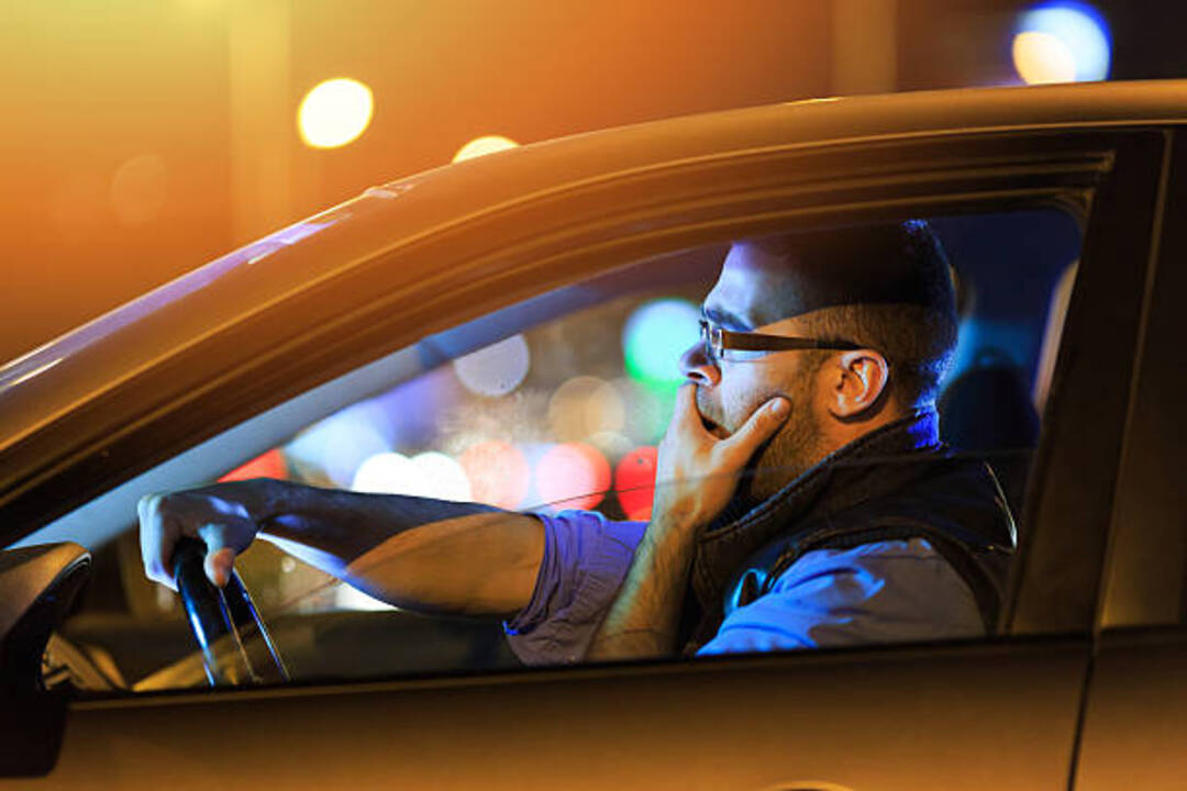A tired driver yawning at the wheel, possibly due to snoring.