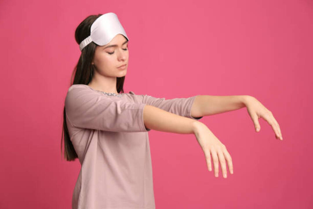 Woman sleepwalking with sleep mask on pink background