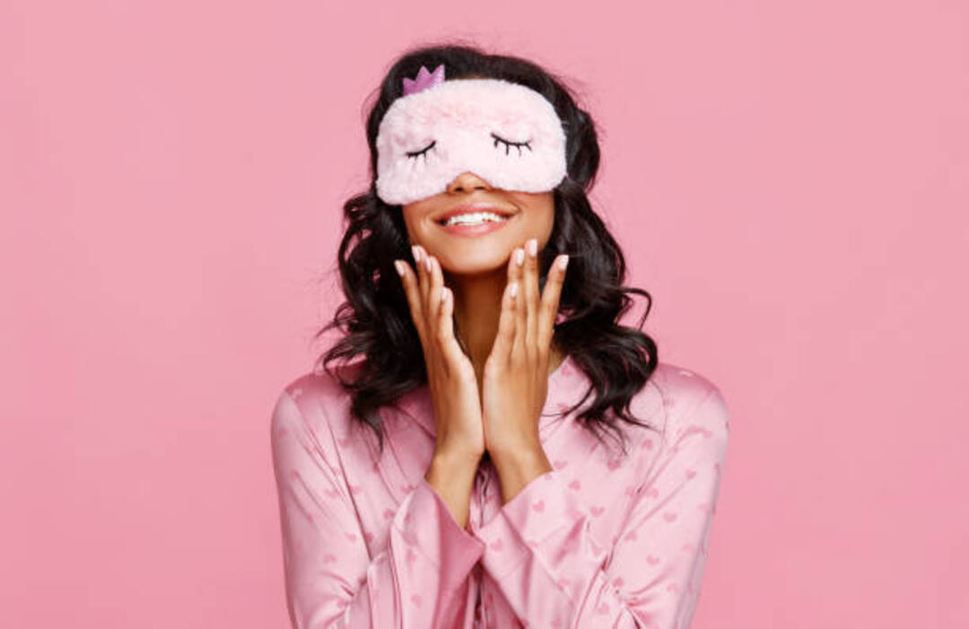 Smiling woman with sleep mask promoting good sleep hygiene.