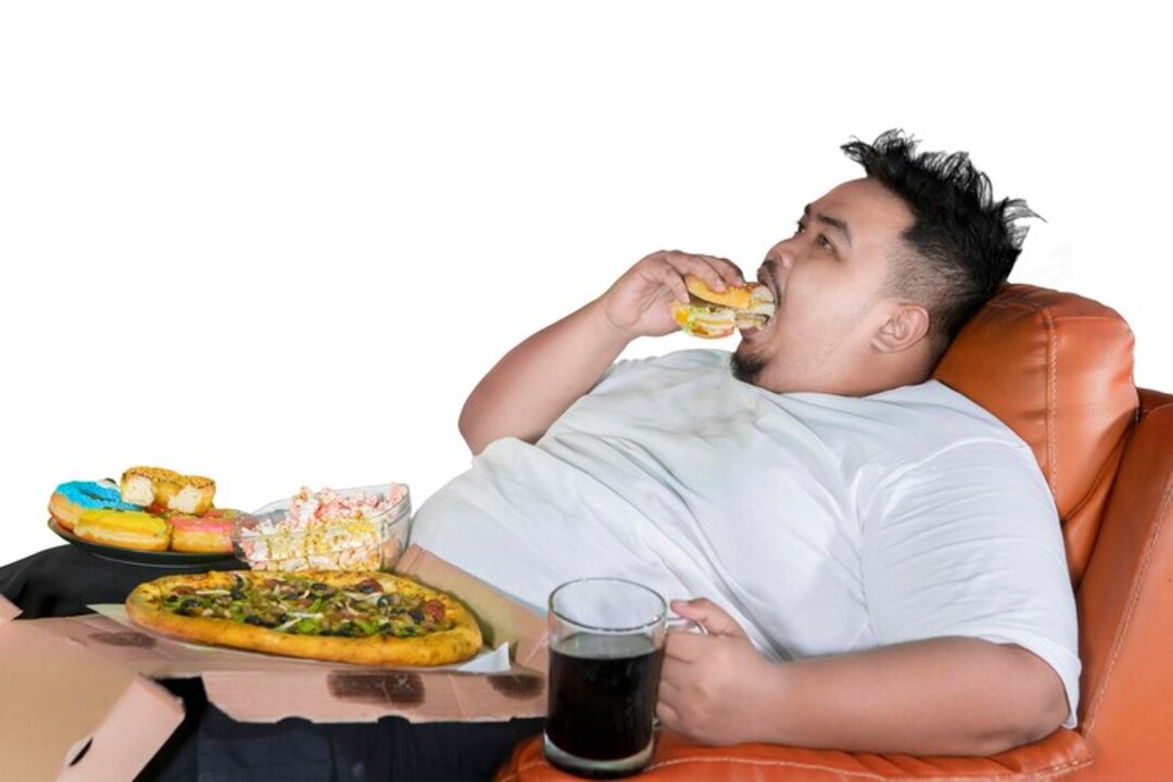 Overweight man eating junk food contributing to weight gain.
