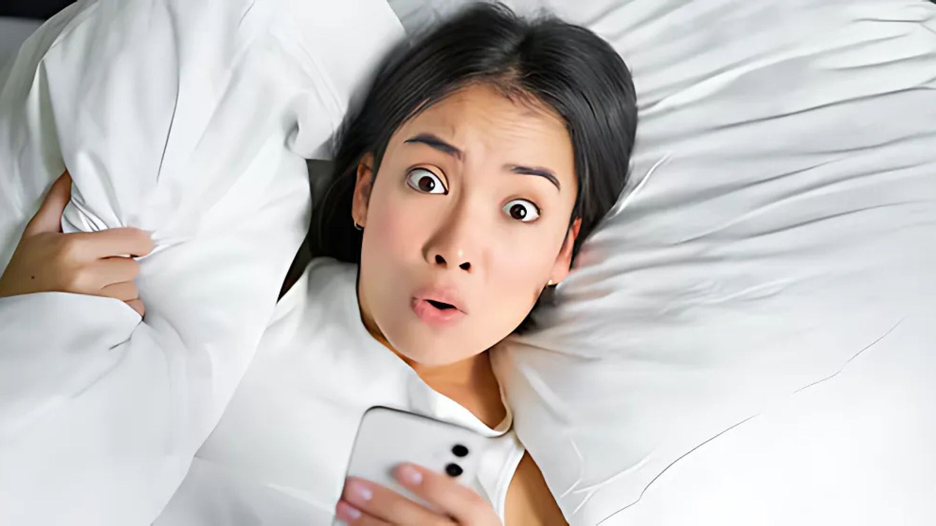 Woman surprised and holding her pillow while using her phone.