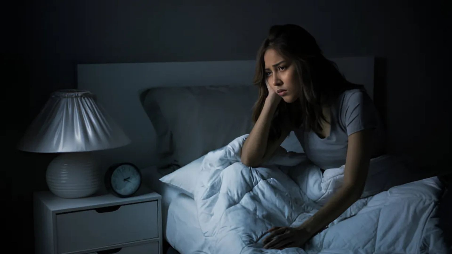 A woman awake in bed, struggling with sleep, looking distressed.