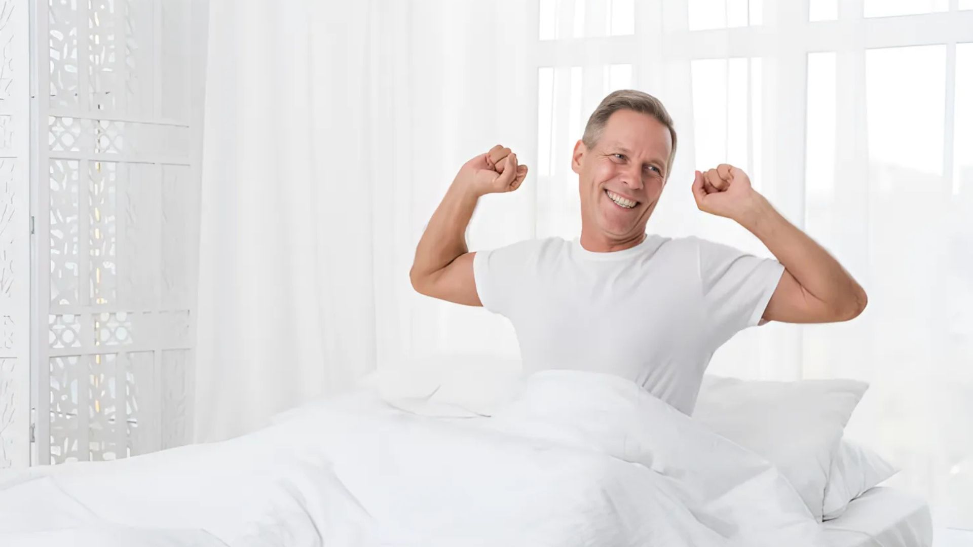 A man smiling and stretching in bed after a good night's sleep.