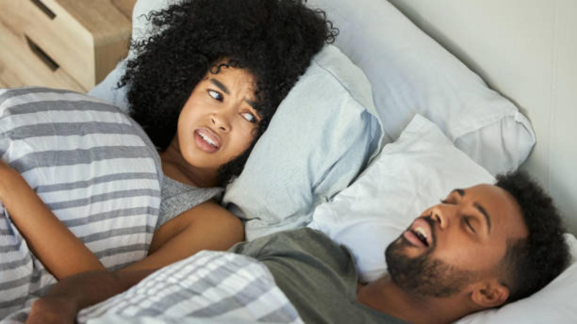 Couple in bed: one partner snores, other shows frustration.